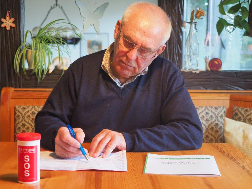 Ein Mann füllt am Küchentisch das Formular für die Rettungsdose aus, daneben steht die rote Dose